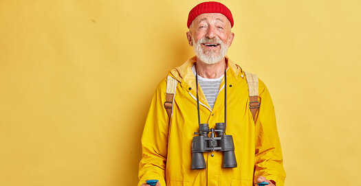 Bärtiger, fröhlich schauender Mann mit roter Mütze und gelbem Regenmantel beim Nordic Walking, gelber Hintergrund