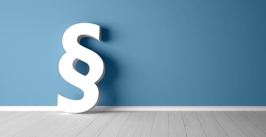 Ein großes Paragraphen-Zeichen lehnt auf dem Holzfußboden an einer blauen Wand