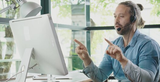 Ein Mann mit Headset spricht über eine Videokonferenz mit Kolleginnen und Kollegen - Foto von Adobe Stock
